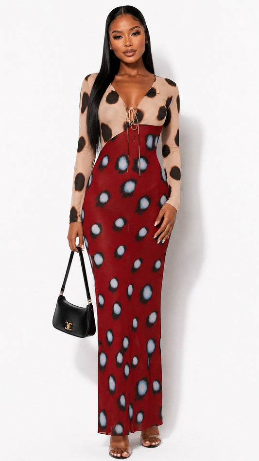 A woman modeling a long-sleeve maxi dress with a beige and black leopard print on the upper bodice and sleeves, and a red skirt section with large black and white spots. She is holding a small black handbag against a plain white studio background.