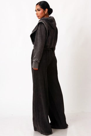 A woman modeling a dark gray hooded sweatshirt and matching wide-leg pants, shown from a side-back angle against a plain white studio background.