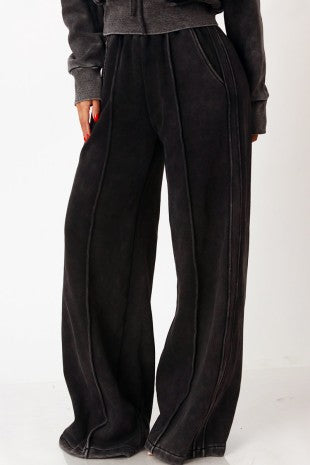Black wide-leg cropped pants with side pockets and a textured fabric, shown on a model wearing a dark gray cropped hoodie against a white studio background.