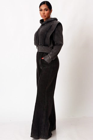 A woman modeling a dark gray cropped hooded jacket with a wide collar and matching wide-leg pants, photographed against a plain white studio background.