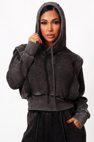 A woman wearing a dark gray washed cropped hoodie with drawstrings and a matching dark gray sweatpants, shown against a plain white background.