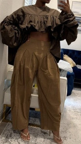 A person takes a mirror selfie wearing a matching two-piece outfit consisting of a brown ruffled off-the-shoulder crop top and high-waisted, wide-leg brown pants, paired with clear high-heeled sandals in a modern indoor setting.